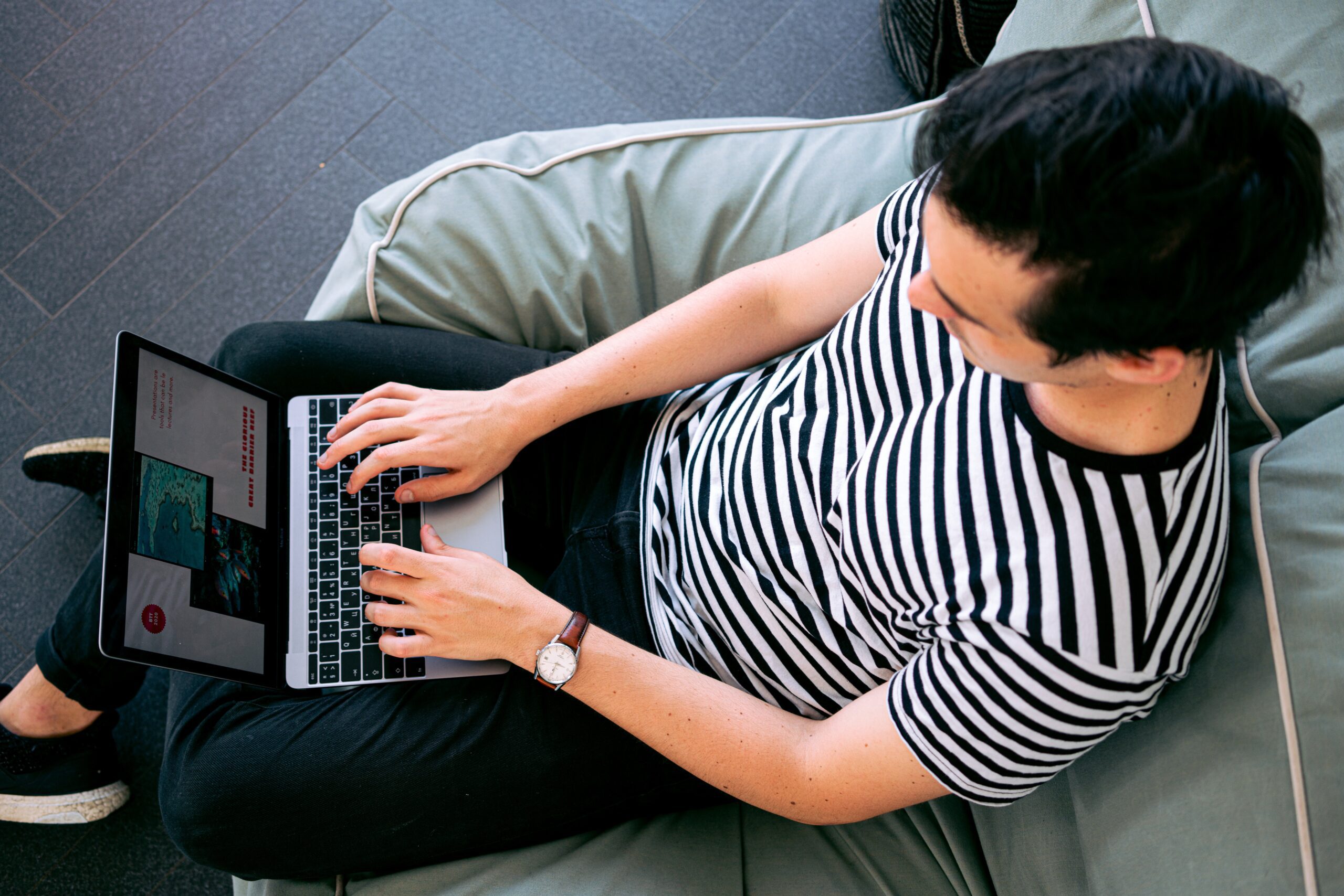 Overhead photo of a man wearing a black and white stripped shirt working on a laptop.