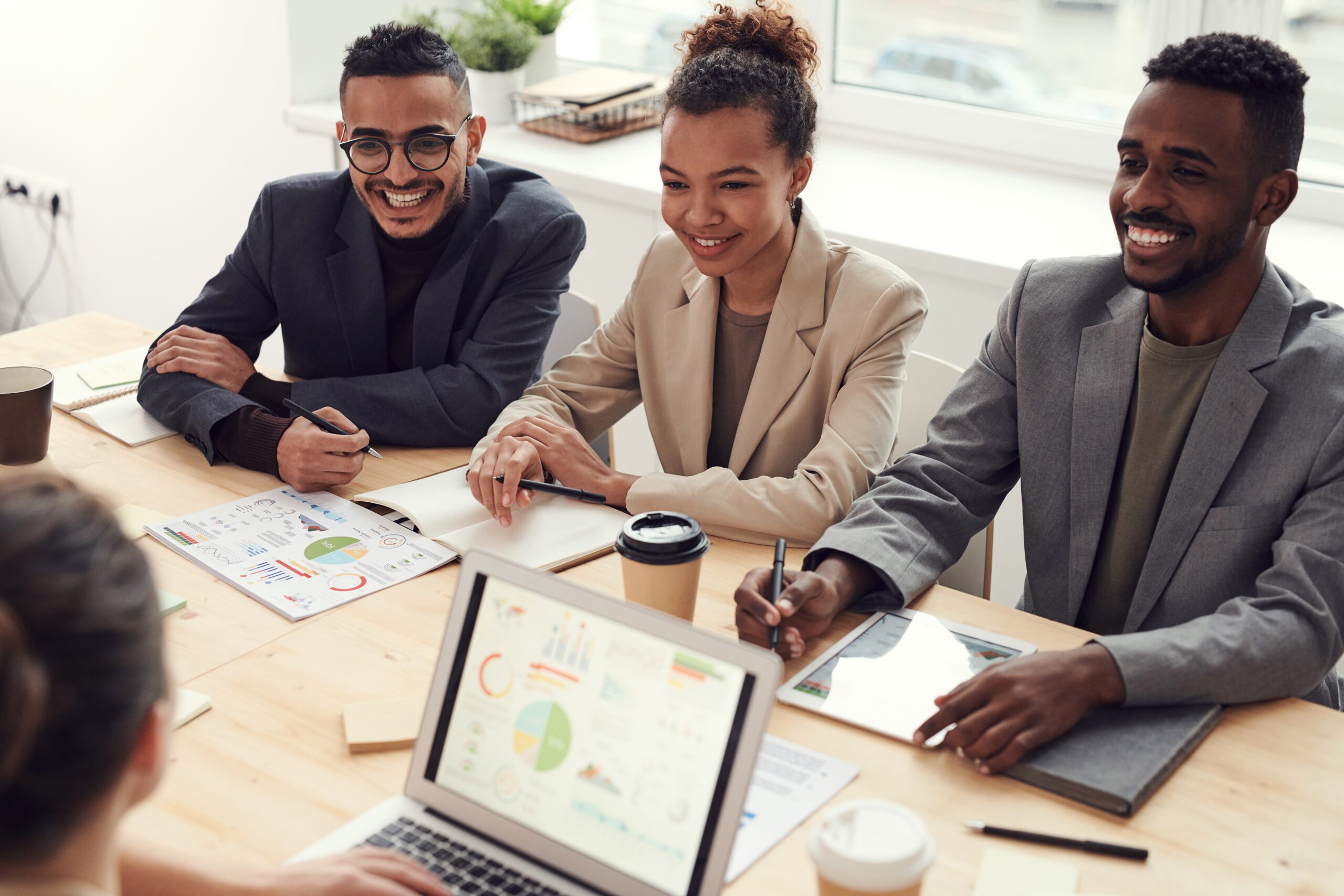 Photo of a businessman, businesswoman, and a businessman sitting across a table from someone else who is looking at their laptop.